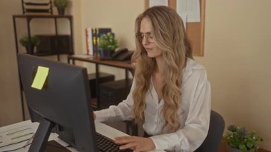 Ofisteki kadın bilgisayarla masada otururken sırt ağrısı çekiyor, iş ortamındaki rahatsızlığı vurguluyor..