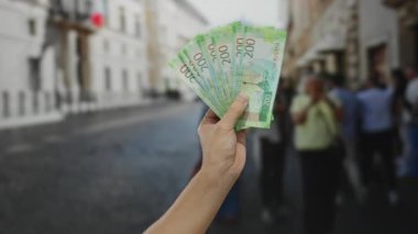 Meşgul şehir caddesinde elinde Rus rublesi tutan adam, arka planda insanlar, açık şehir ortamında finans temasını vurguluyor..