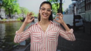 Kadın eli, Amsterdam 'da güneşli kanal sokağında su ve binalarla birlikte tamam işareti gösteriyor. Onaylandı.