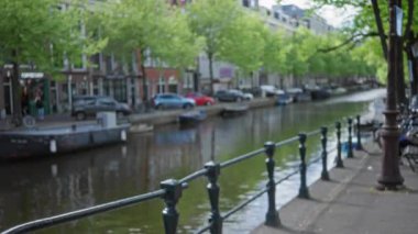Güneşli bir günde yemyeşil ağaçların altında Amsterdam 'ın canlı çizgili kanallarının ve geleneksel mimarisinin bulanık görüntüsü Hollanda' daki hareketli şehir yaşamını yakalıyor..