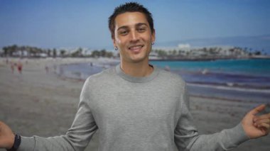 Genç İspanyol adam açık gökyüzünün altında kumsalda gri kazaklı iki tarafı da işaret ediyor. Kararsızlık..