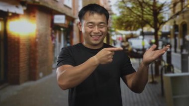 Genç adam, tuğla binalar ve geçen bisikletlerle çevrili, hareketli, güneşli bir kaldırım taşı caddesini işaret ediyor..