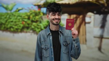 Açık havada Fransız pasaportu taşıyan bir adam canlı, güneşli bir şehir zeminine karşı sıradan bir kot ceketle gülümsüyor..