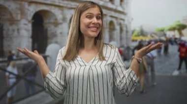 Kalabalık bir caddede antik kolezyumun önünde kollarını açmış gülümseyen genç bir kadın..