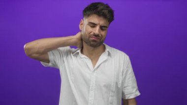 Beyaz tişörtlü, boyuna dokunan ve mor stüdyoda somurtan yumuşak ışıkla aydınlatılan Latin asıllı genç adam..