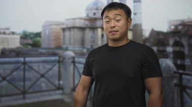 Siyah tişörtlü adam şehir siluetine tepeden bakan çatı balkonunda kamerayı işaret ediyor..