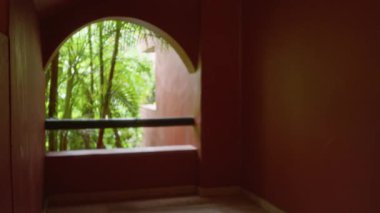 Tropik tatil köyü koridoru, kemerli bir pencereden yemyeşil, bulanık ve çözünmüş bir görüntüde sakin ve lüks bir açık hava ortamı yaratıyor..