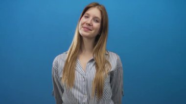 Kafasını eğen ve uzun saçlı, parlak mavi stüdyoda çizgili gömlek giyen, sıcak özgüvenli bir kadın..