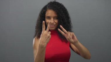 Stüdyo ortamında izole edilmiş gri arka planda hashtag işareti yapan bir kadın gülümsüyor. Modern sosyal medya teması için kıvırcık saç stilini ve canlı kırmızı bluzunu geliştiriyor.
