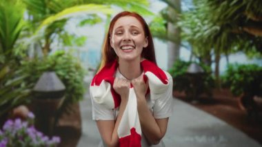 Canlı yeşilliklerle çevrili, yemyeşil bir parkta kırmızı eşarpla gülümseyen bir kadın, açık havada neşe ve sıcaklık ifade ediyor..