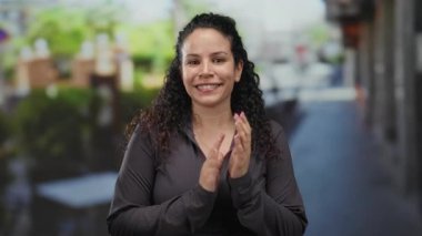 Terasta neşeli bir şekilde gülümseyen kadın, arka planda canlı bir sokak bulunan canlı, kentsel bir sahneyi yakalar, mutluluk ve rahatlamış bir ortam hissi taşır..