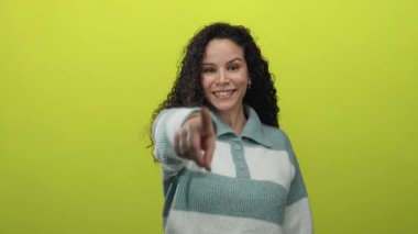 İzole edilmiş sarı arka planda gülümseyen, kıvırcık saçlı, çizgili süveter giyen, arkadaş canlısı bir ifade sergileyen bir kadın..