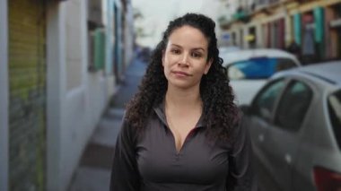 İspanyol kadın, şehir dışında park etmiş arabalarla sokakta güçlü bir jest yapıyor. Güvenini ve gücünü belli bir ifadeyle gösteriyor..