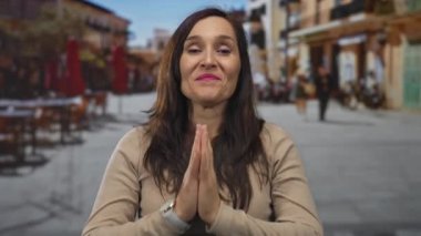 Güneşli bir sokakta yüzü bulanık kafeler ve arka planda insanlar olan bir kadın gülümsüyor.