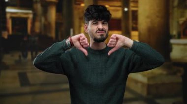 Sakallı genç bir adam müzenin içinde dikilirken baş parmak hareketi yapıyor..