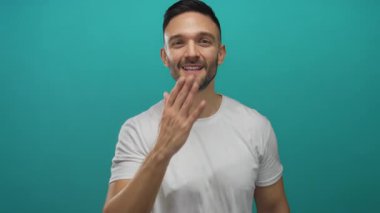 Beyaz gömlekli genç İspanyol bir adam öpücükler saçar ve parlak mavi bir arka plana gülümser. Olumlu duygular ve karizma gösterir..