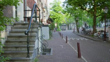 Güneşli bir günde bulanık Amsterdam Caddesi 'nde merdivenler, bisikletler ve yemyeşil ağaçlar..