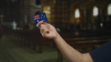 Kilisenin içinde küçük bir Avustralya bayrağı tutan beyaz bir adam. Nakış işliyor. İç mekanlardaki kültürel sembolizmi vurguluyor..