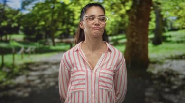 Çizgili gömlekli genç kadın, ağaçların arasındaki ormanda gözlük takarak samimi bir anı görüntülemek için gözlerini kapatıyor..