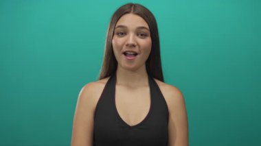 Genç bir kız göğsüne yakın el sıkışıyor gözleri kapalı ve stüdyoda tatlı tatlı gülümsüyor; sakin..