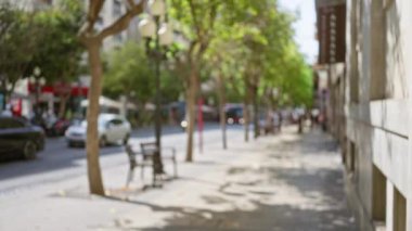 Arka planda insanlar, arabalar, bisikletçiler, ağaçlar ve dükkanların olduğu bir şehir manzarası bulanık