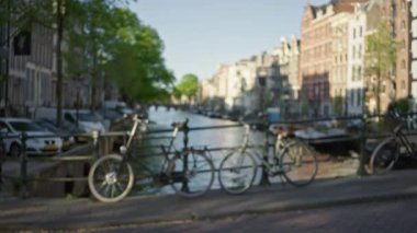 Ön planda bisikletler ve arka planda tarihi binalarla manzaralı bir kanalda yürüyen iki kadının bulanık görüntüsü..