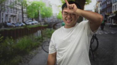 Adam beyaz bir gömlek giyerken park halindeki bisiklet ve tuğla binalarla dolu caddede kanalı işaret ediyor..