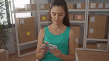 Kadın depolama binasındaki karton kutular arasında paket takibi için akıllı telefonu dinliyor; memnuniyet.