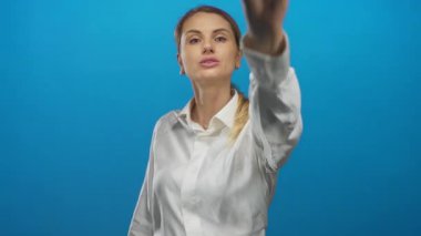 Kalbi olan ve stüdyoda kameraya bakan, mavi arka planda, ifadesini ve iletişimini etkili bir şekilde gösteren bir kadın..