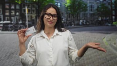 Elinde kameraya yakın bir kredi kartı olan bir kadın kaldırım taşı şehir caddesinde el kol hareketi yaparken gözlük takıyor, ödeme düş kırıklığı yaşıyor..