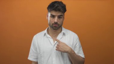 Parmakla göğsünü gösteren turuncu stüdyo ışıkları ve tarafsız yüz ifadesi olan bir adam..