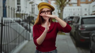 Kırmızı saçlı, gözlüklü, sarı şapkalı, kırmızı gömlekli, şehir modasını ve duygularını canlı bir şekilde gözler önüne seren bir kadın..