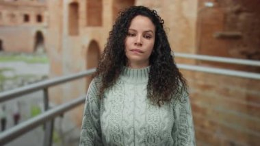 Roma harabelerinde şakacı hareketler yapan bir kadın eski mimari ile arka planda gelişigüzel giyinmiş genç bir İspanyol kadını sergiliyor..