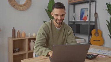 İspanyol adam rahat bir oturma odasında neşeyle dans ediyor. Dizüstü bilgisayarla etkileşim kurarken kutlama yapıyor. Etrafı gitar ve raflarla çevrili..