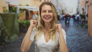 Sarışın genç bir kadın şehir sokaklarında neşeyle gülümserken, neşeli şehir manzarasıyla çevrili mutluluk ve enerjiyi somutlaştırıyor..