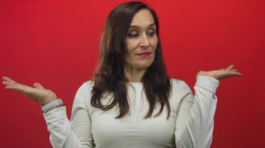 İfadesi sorgulanan kadın, kararsızlık ve merakla bezenmiş beyaz gömlekli, soyutlanmış kırmızı arka plana karşı duruyor..