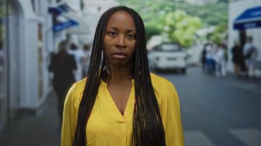 Şehir manzarası bulanık ve yoldan geçen yayalarla çevrili, uzun örgülü saçları ve dalgın bir ifadeyle bir kadın, şehir caddesinde dikiliyordu..