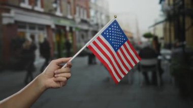 Şehir sokaklarında Amerikan bayrağı tutan adam, şehir geçmişi bulanık ve yayaları olan bir açık alanda vatanseverliği ve milliyeti vurguluyor..