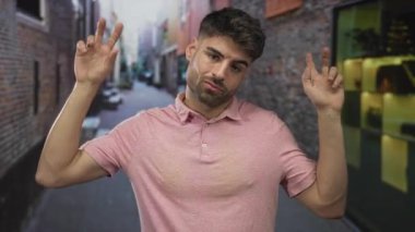 Hispanik adam şehirdeki dar tuğladan sokak üzerinde parmaklarıyla tırnak işareti yapıyor; şüphecilik.