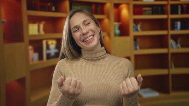 Genç sarışın kadın kütüphanede elleri ile işaret eder; davet hoş geldiniz.
