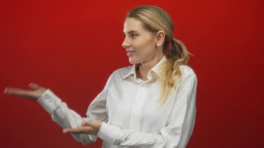 Cesur kırmızı bir arkaplan karşısında elleri açık duran bir kadın stüdyo ortamında kendine güvenen ve profesyonel bir tavır sergiliyor..