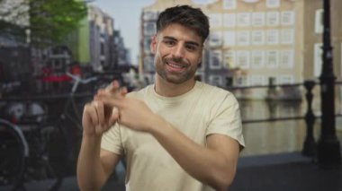 Genç İspanyol adam, kanal binalarının yanındaki kaldırım taşı sokakta birbirine dolanmış parmakları olan bir hashtag işareti yapıyor..