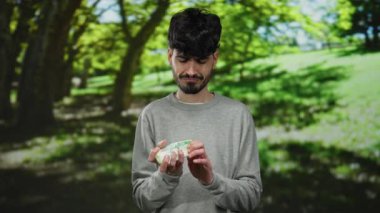 Parktaki Rus rublelerini sayan bir adam, yemyeşil yemyeşil ile çevrili, düşünceli bir ifadeyle sakin açık havada tefekkür ediyor..