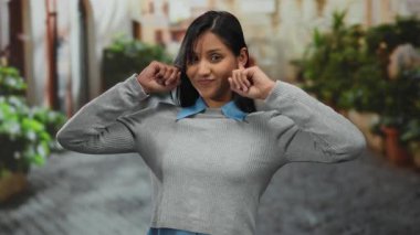 Yeşillik ve tarihi mimari ile çevrili, neşe ve kaygısızlığı temsil eden canlı sokak ortamında kulakları tıkayan bir kadın..