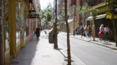 Bulanık yayalar ve Bokeh etkisine sahip Avrupa sokaklarının odak dışı görüntüsü şehir mimarisi ve mağazalar yoluyla güneş ışığının filtrelediği kentsel yaşamı vurguluyor.