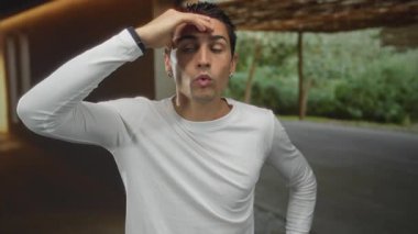 Modern odada beyaz gömlekli genç İspanyol bir adam doğal arka planda hafif ışıklandırmanın altında ifade edici bir yüzle konuşuyor.