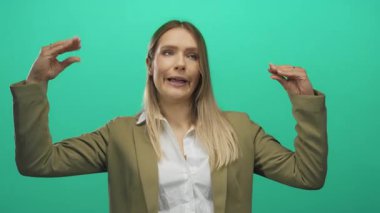 İzole edilmiş yeşil arkaplan karşısında el kol hareketi yapan kadın spor ceket ve beyaz gömlek giyip iletişim ve ifade öneriyor..
