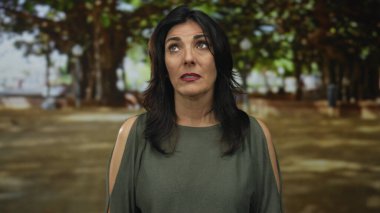 Ormanda, yeşil dalların arasında yüzleri birbirine çarpan kadın, sessiz yalnızlığı yansıtıyor..