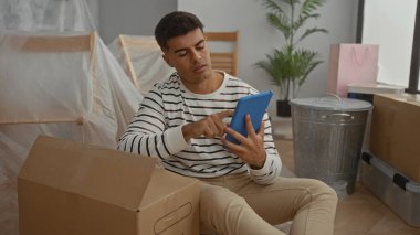 Genç adam yeni bir evde oturuyor. Etrafı kutularla çevrili. Oturma odasında, yüzünde rahat bir ifadeyle tablet kullanıyor..