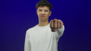 Uzun kollu kurdeleli gömlek giyen gümüş çerçeveli gözlüklü adam stüdyoda ileri doğru sıkılmış bir yumruk gösteriyor..